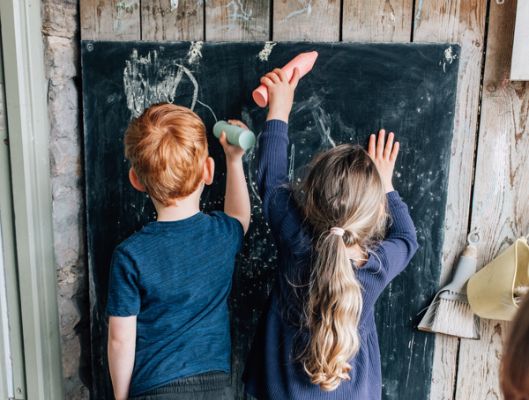 two children drawing on a black chalk board